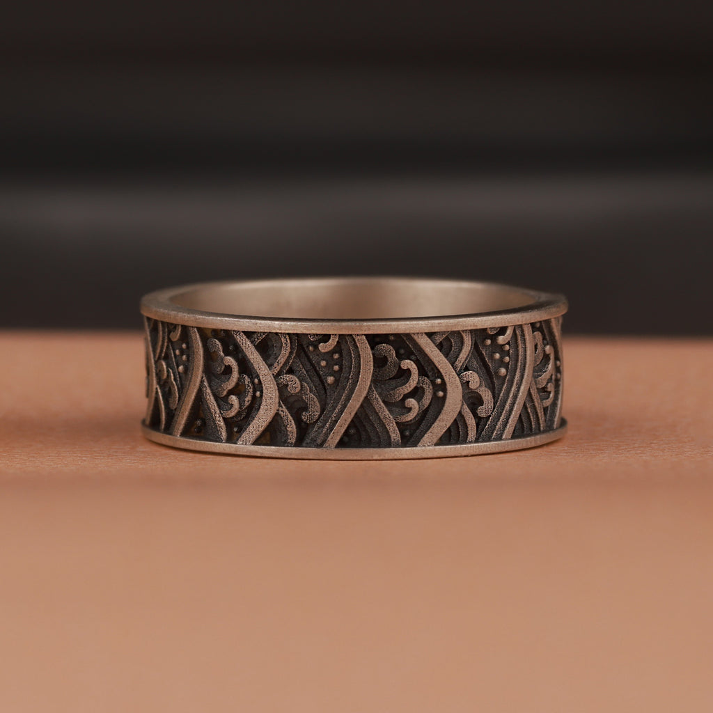 Silver ring with intricate waves patterns on a brown surface