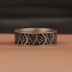 Silver ring with intricate waves patterns on a brown surface