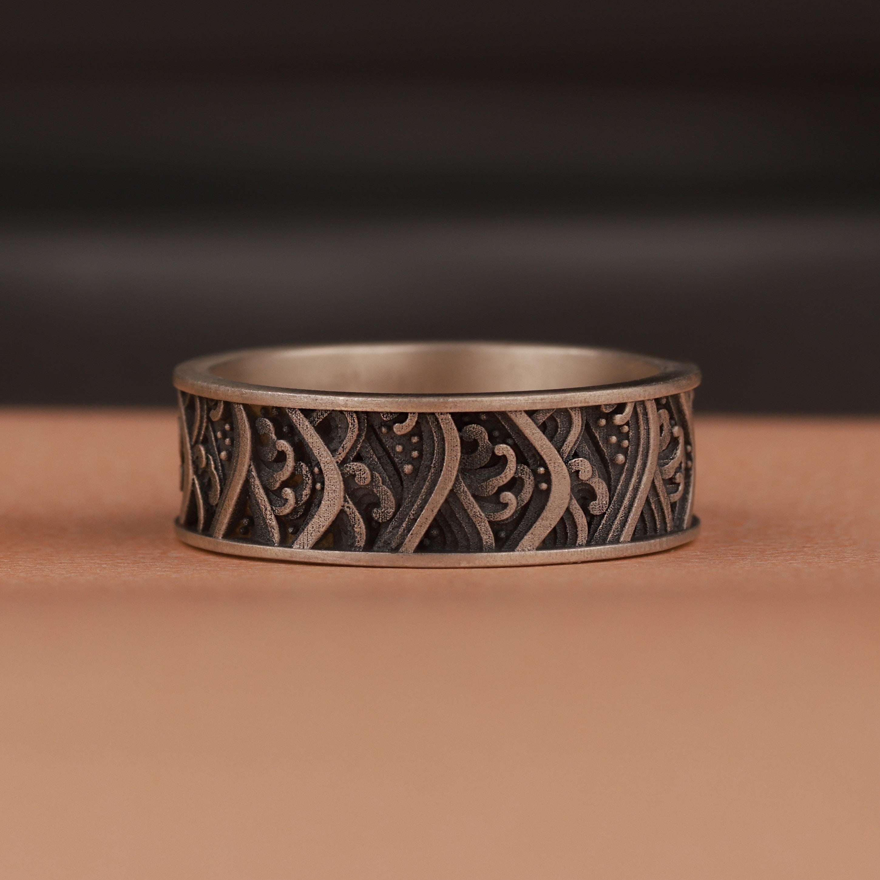Silver ring with intricate waves patterns on a brown surface