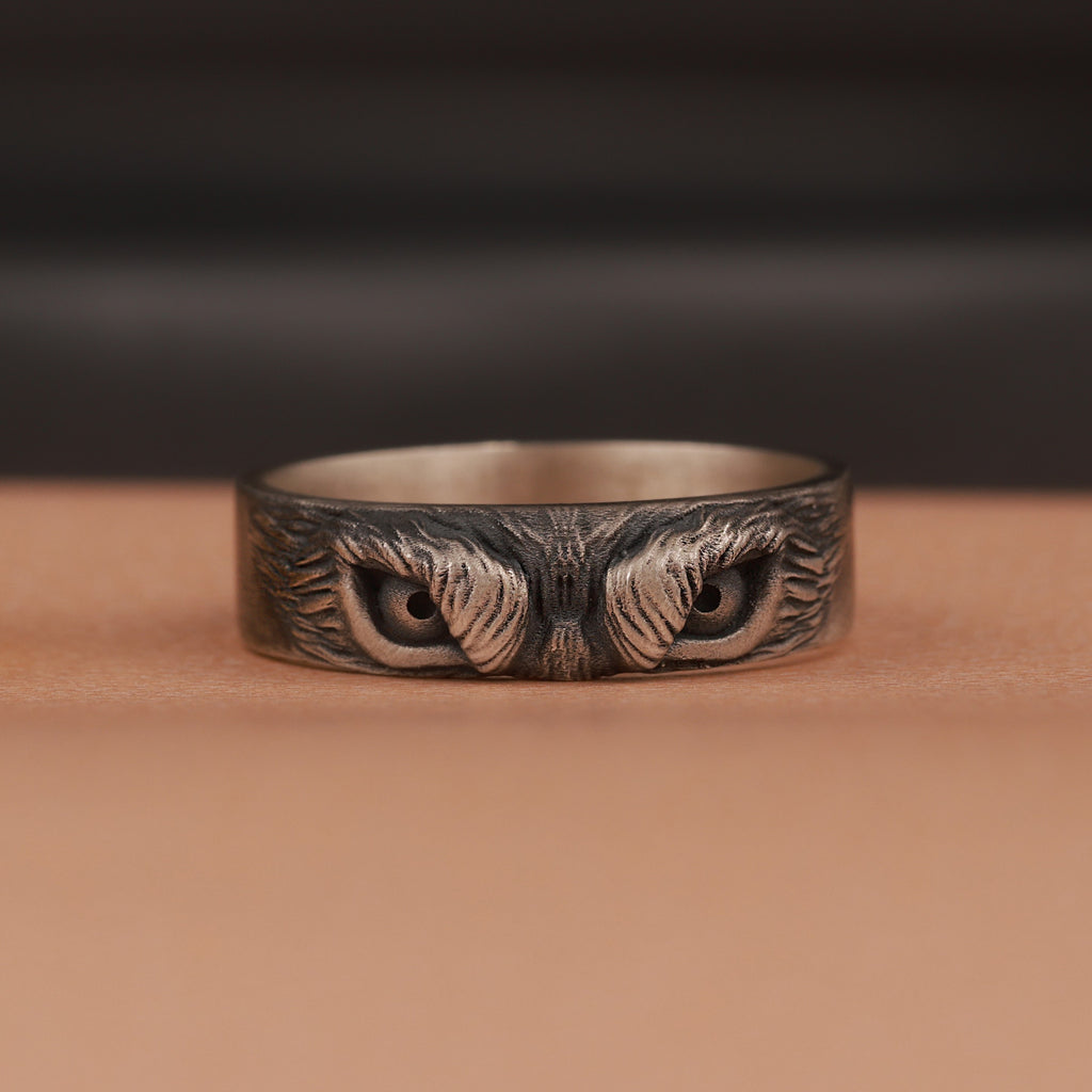 Silver ring with intricate owl eyes design on a brown surface