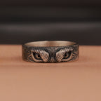 Silver ring with intricate owl eyes design on a brown surface
