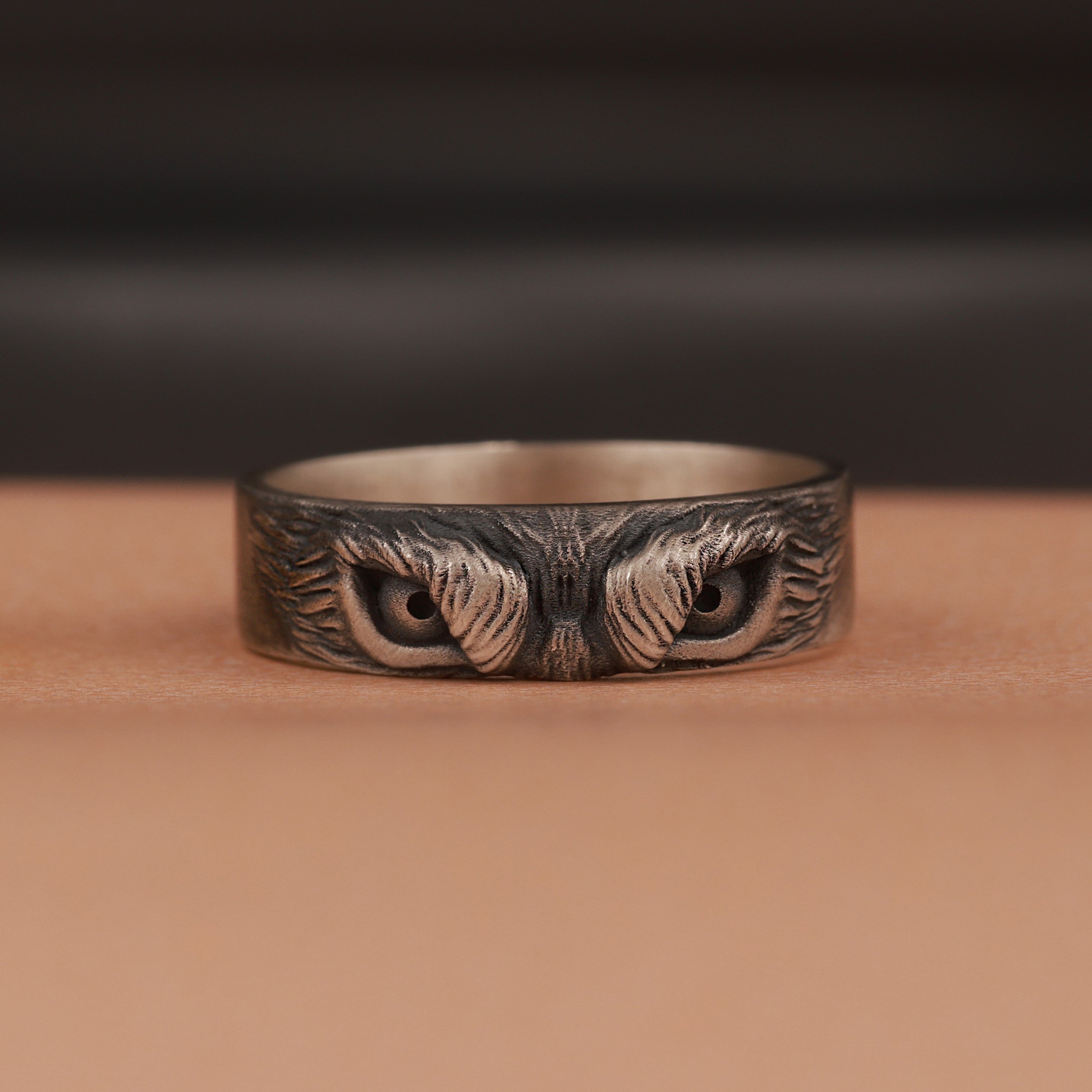 Silver ring with intricate owl eyes design on a brown surface