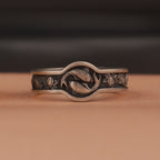Silver ring with fish and lotus designs on a brown background