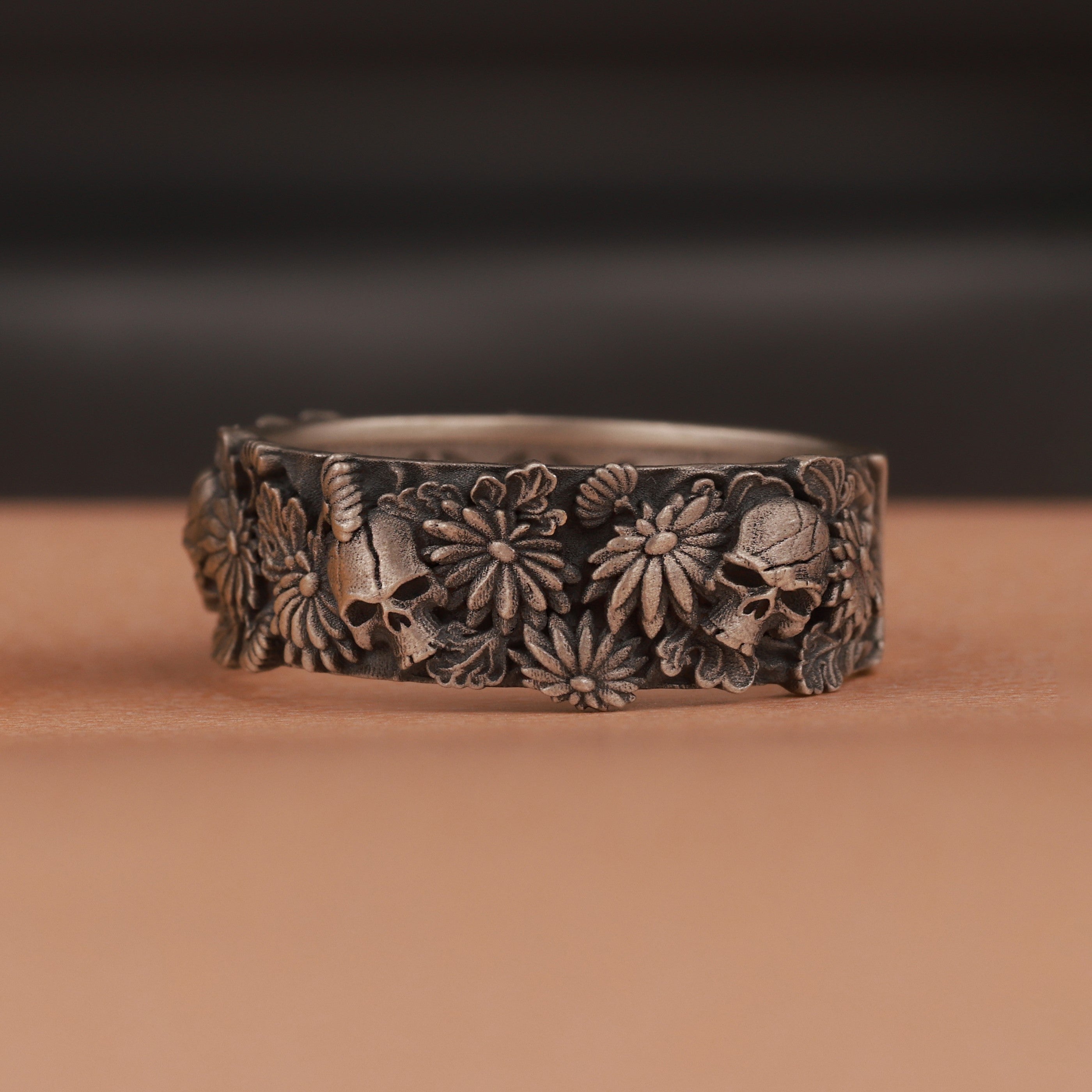 Silver band with skull floral patterns on a brown surface