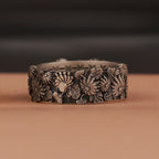 Decorative oxidized silver band with floral patterns on a brown surface