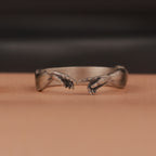 Silver ring with a design resembling 'The Creation of Adam' on a brown background