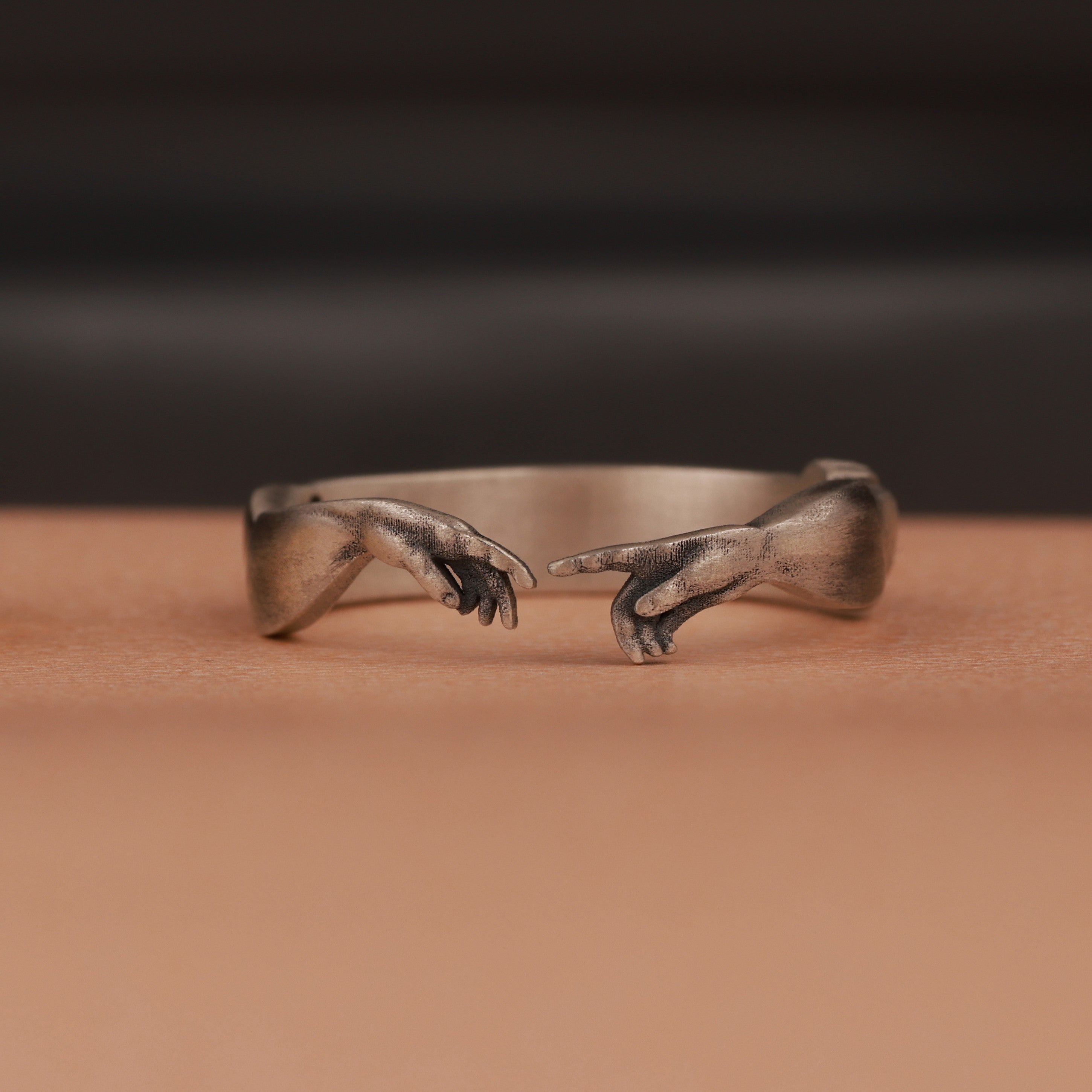 Silver ring with a design resembling 'The Creation of Adam' on a brown background