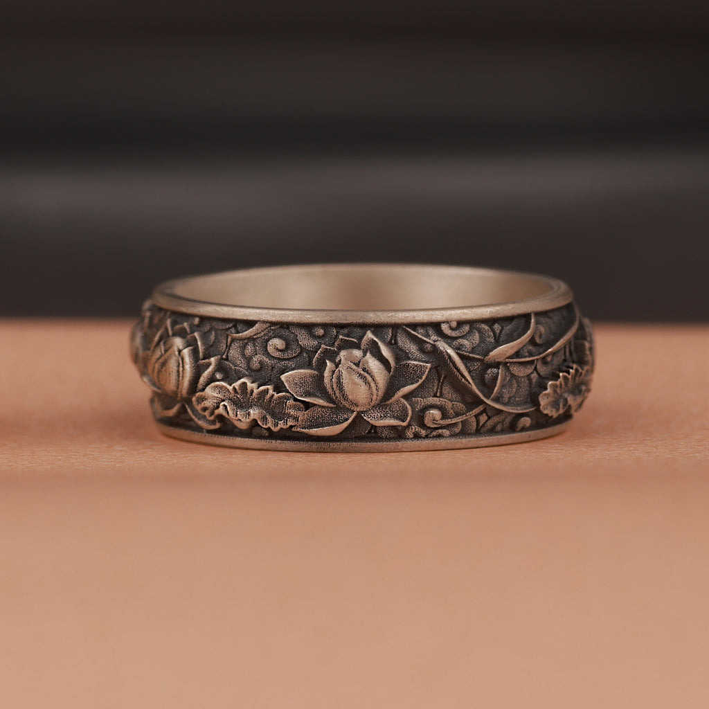 Silver ring with intricate floral patterns on a brown background