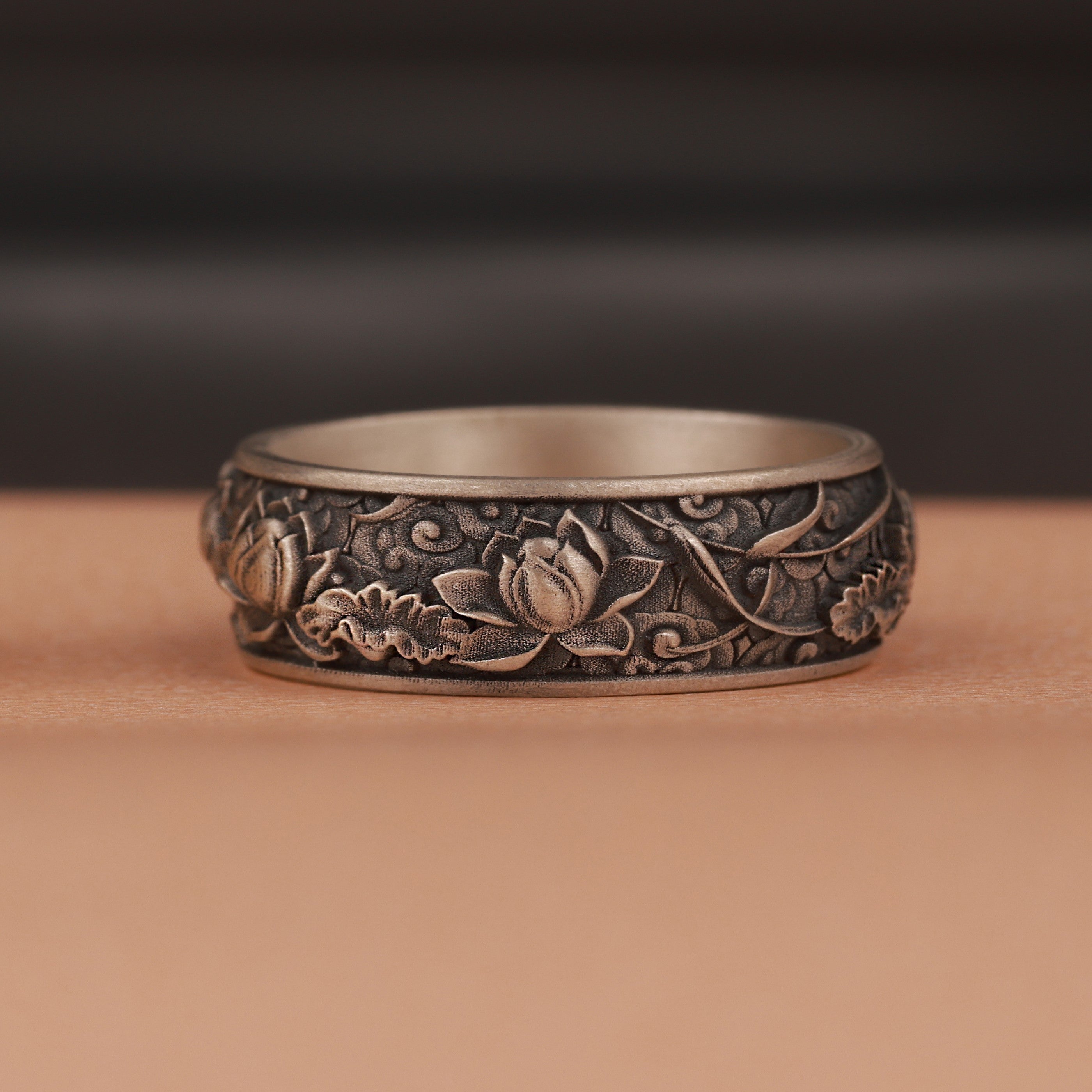 Silver ring with intricate floral patterns on a brown background