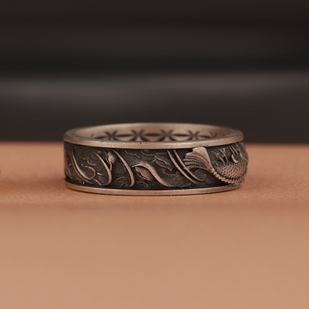 Decorative silver ring with intricate fish  designs on a brown surface