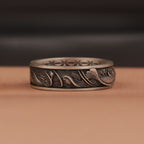 Decorative silver ring with intricate fish  designs on a brown surface