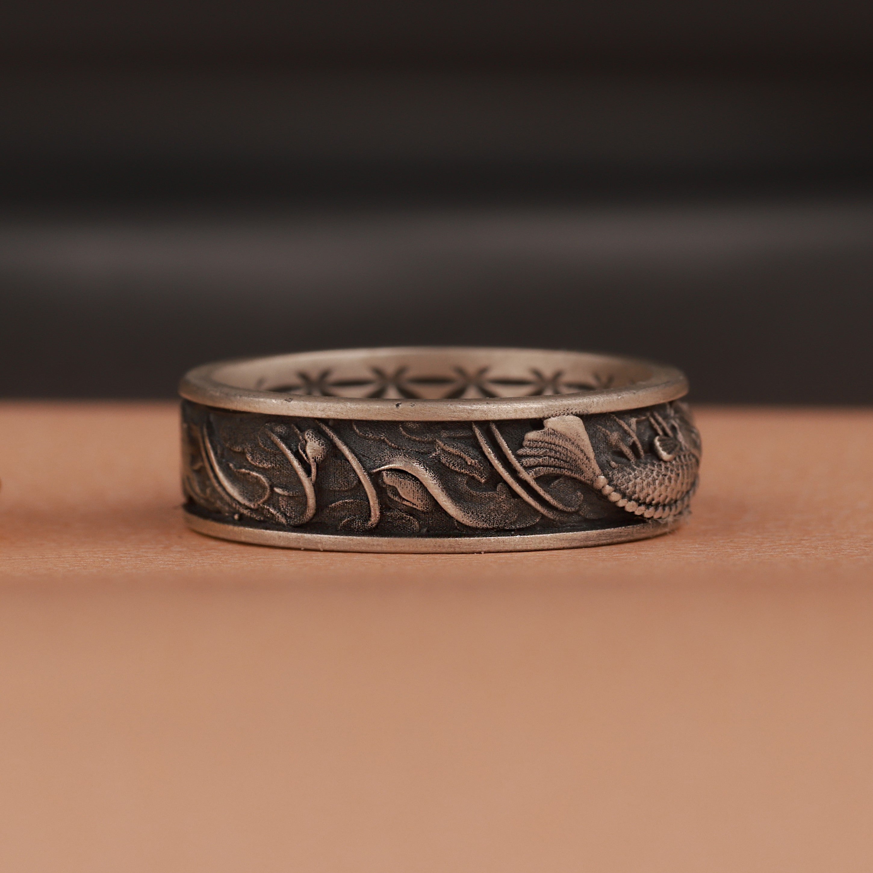 Decorative silver ring with intricate fish  designs on a brown surface