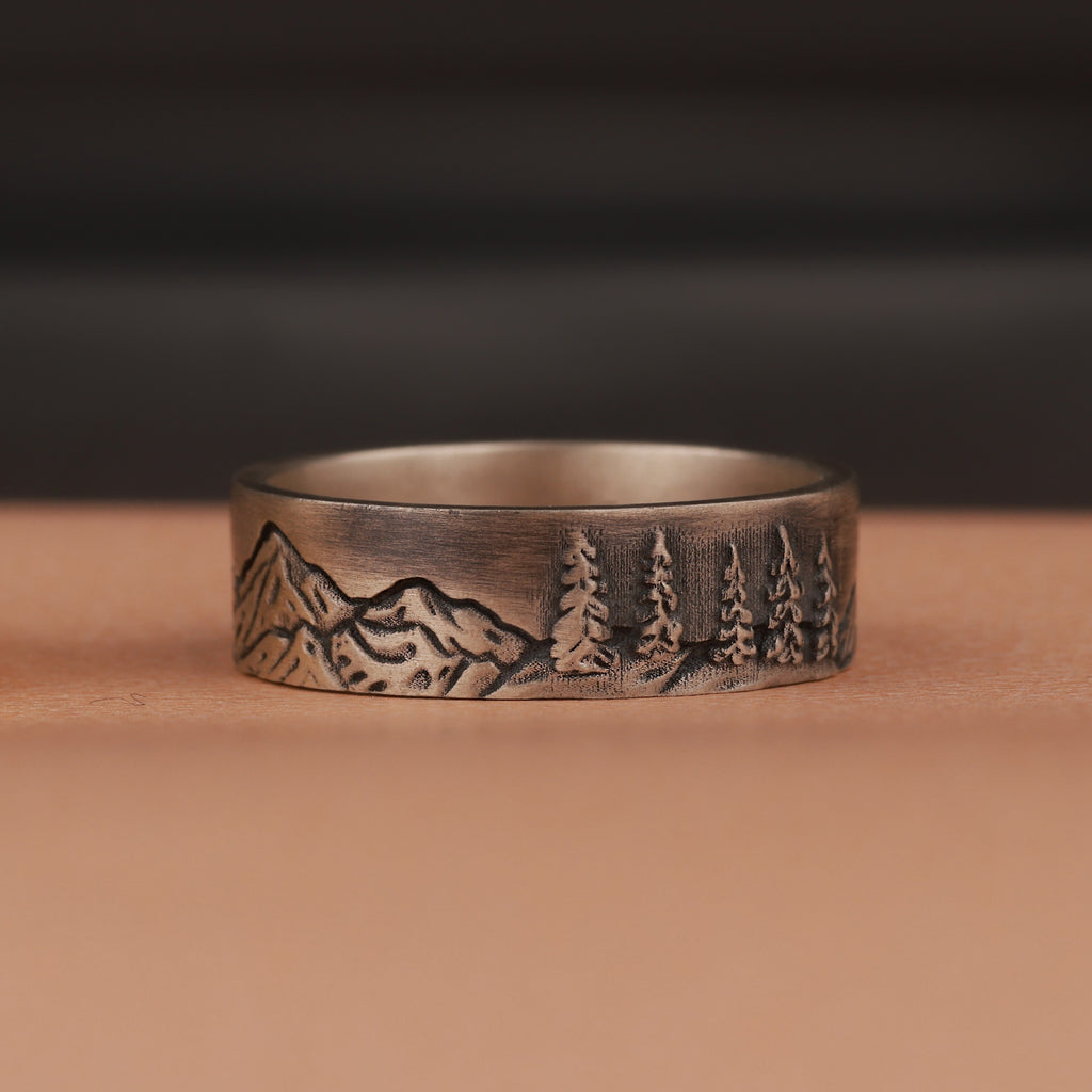 Oxidized silver ring with mountain and tree engraving on a brown surface