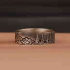 Oxidized silver ring with mountain and tree engraving on a brown surface