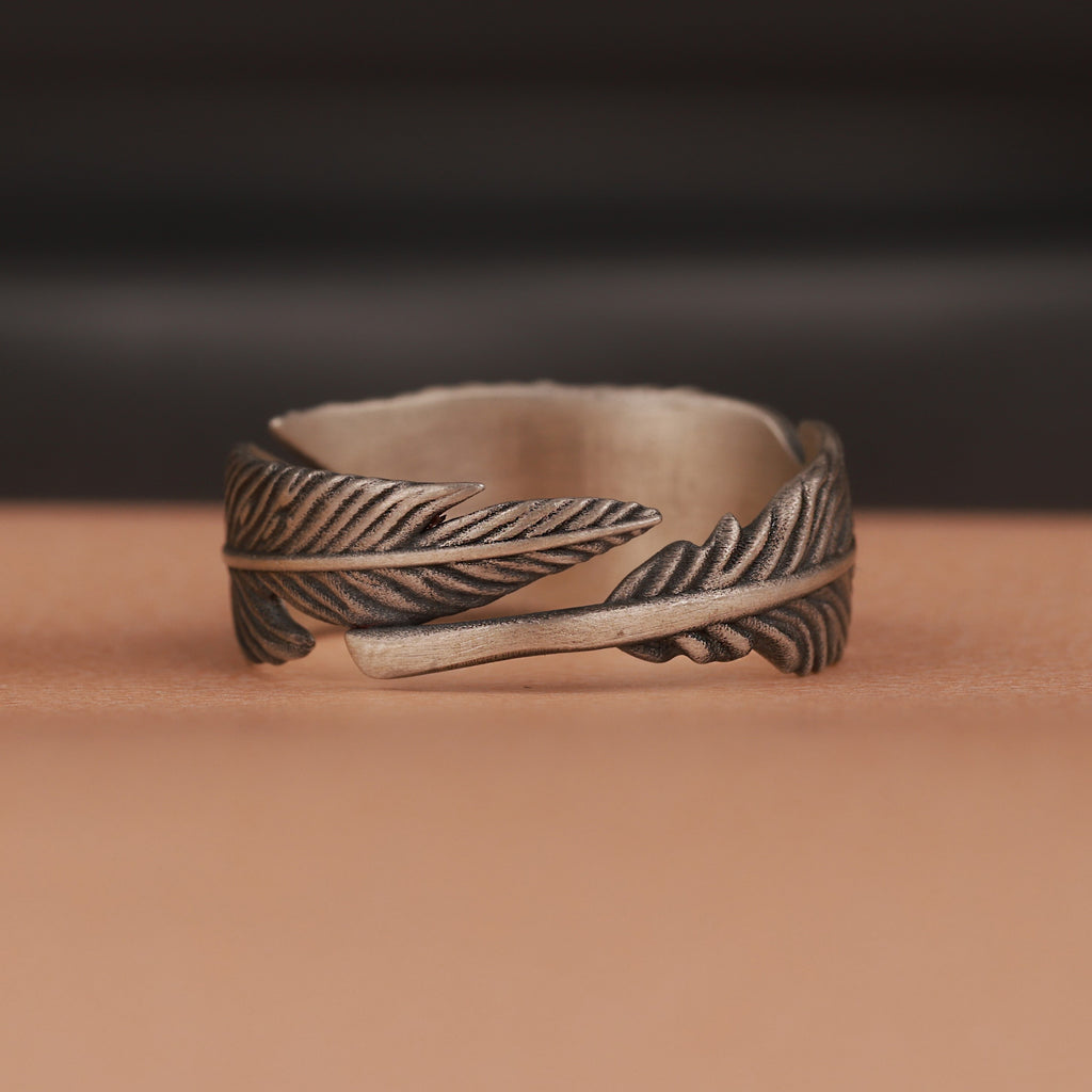 Oxidized silver feather-shaped ring on a brown surface with a blurred dark background
