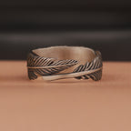 Oxidized silver feather-shaped ring on a brown surface with a blurred dark background