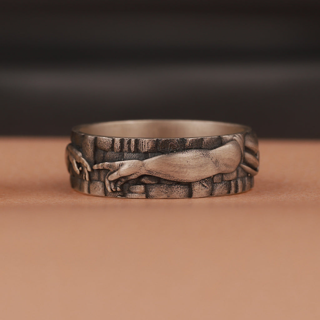 Oxidized band ring with engraved creation of Adam design on a brown background