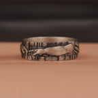 Oxidized band ring with engraved creation of Adam design on a brown background