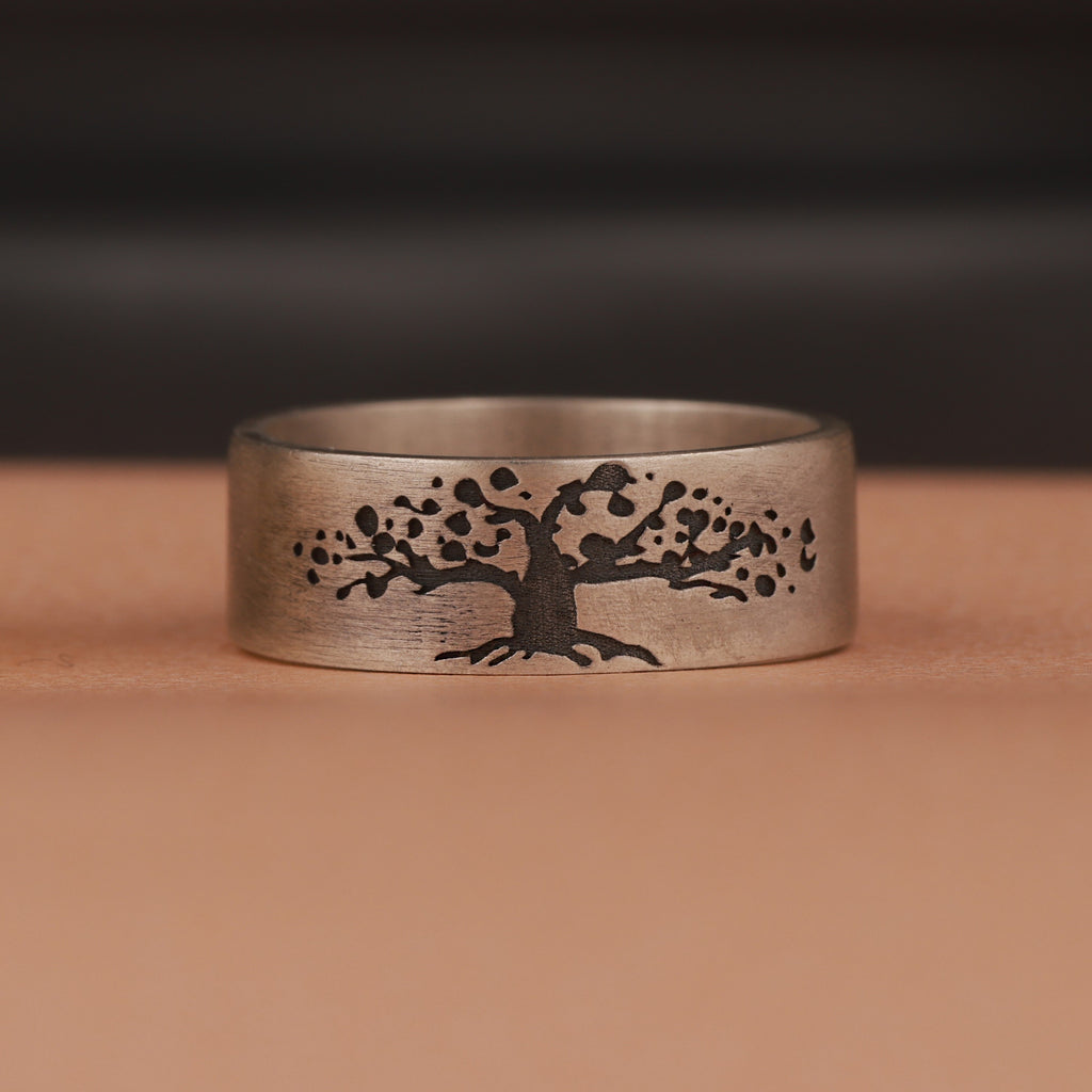 Silver ring with an engraved tree design on a brown background