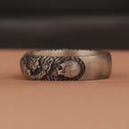 Silver ring with skull and floral design on a brown surface