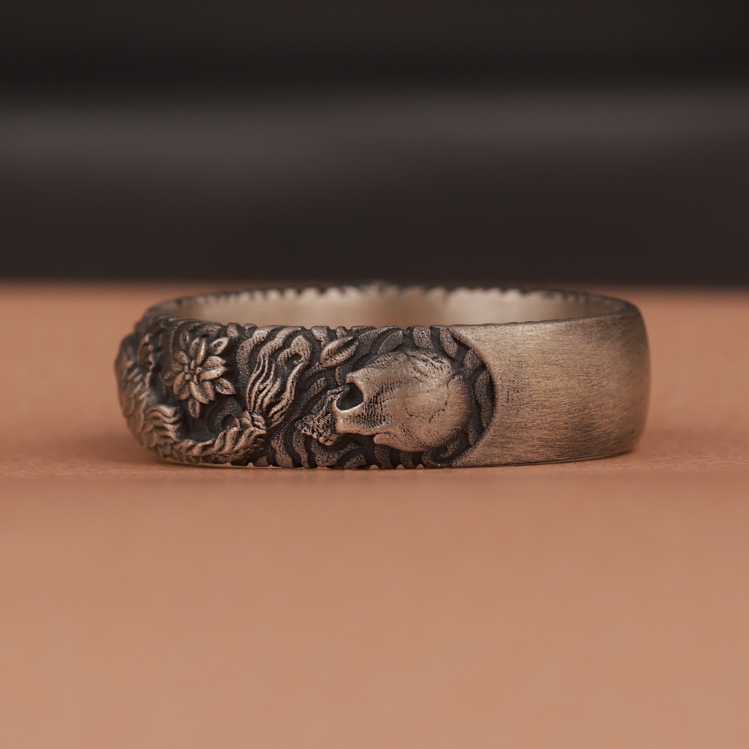 Silver ring with skull and floral design on a brown surface