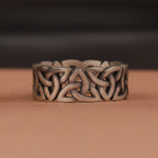 Silver Celtic knot ring on a brown surface with a dark background