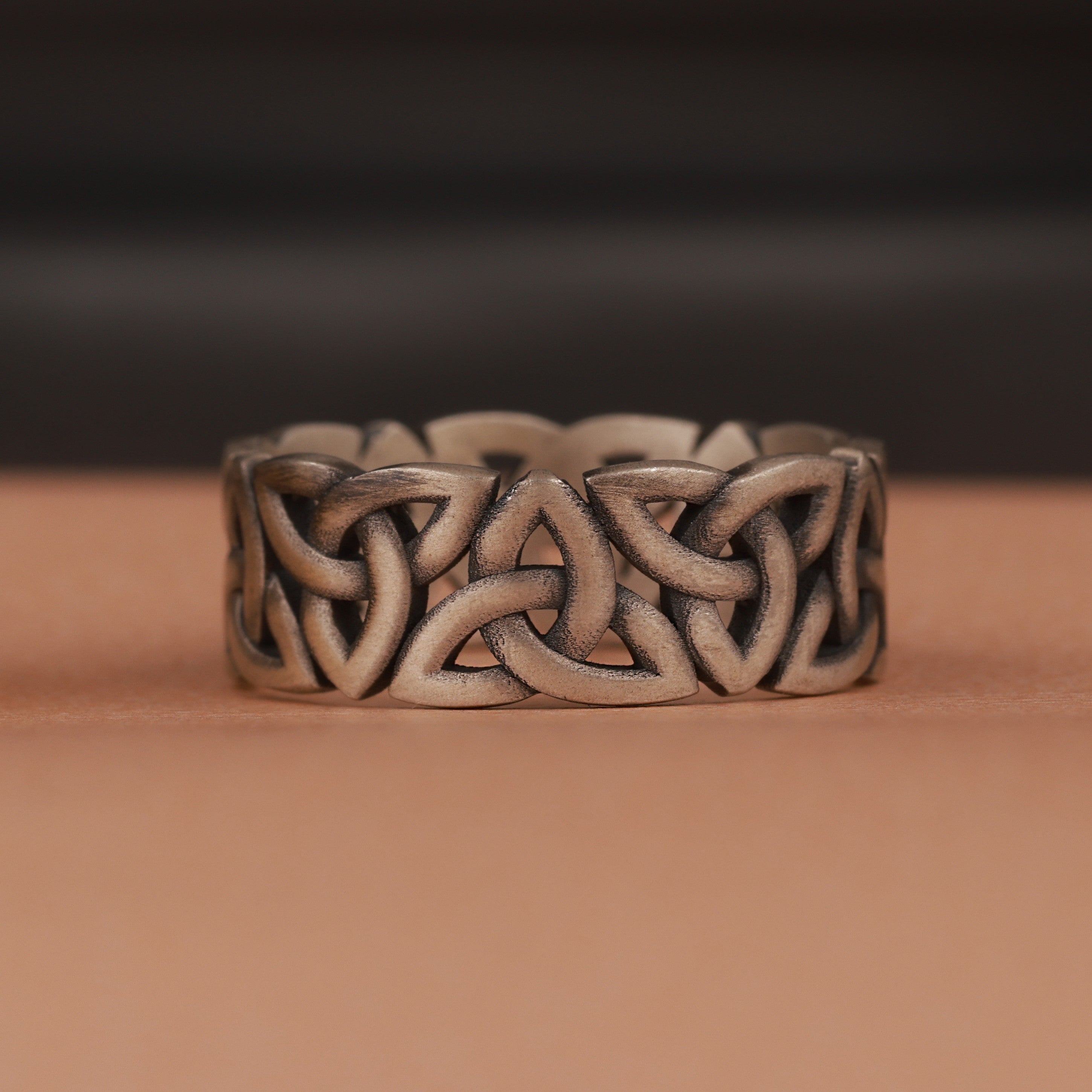 Silver Celtic knot ring on a brown surface with a dark background