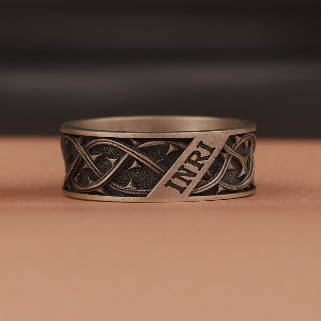 Oxidized silver ring with intricate design and 'INRI' engraving on a brown background
