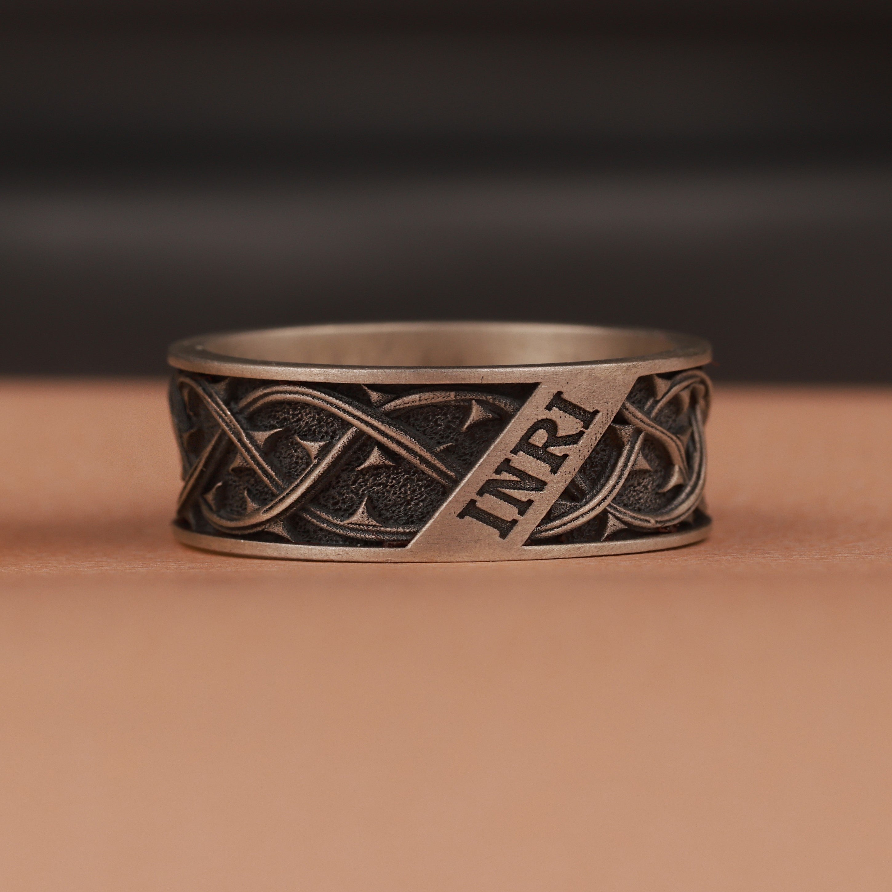 Oxidized silver ring with intricate design and 'INRI' engraving on a brown background