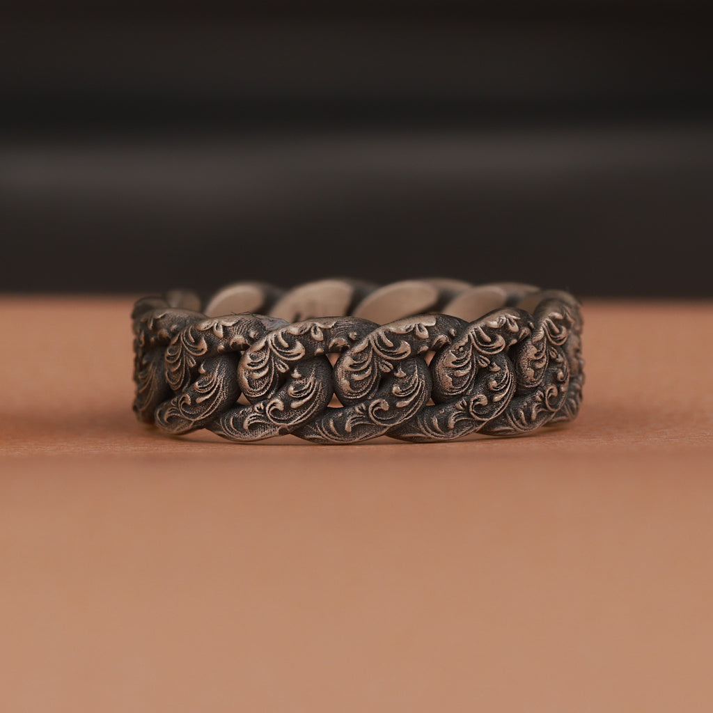 Floral silver chain ring on a brown surface with a blurred black background