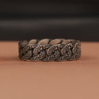 Floral silver chain ring on a brown surface with a blurred black background