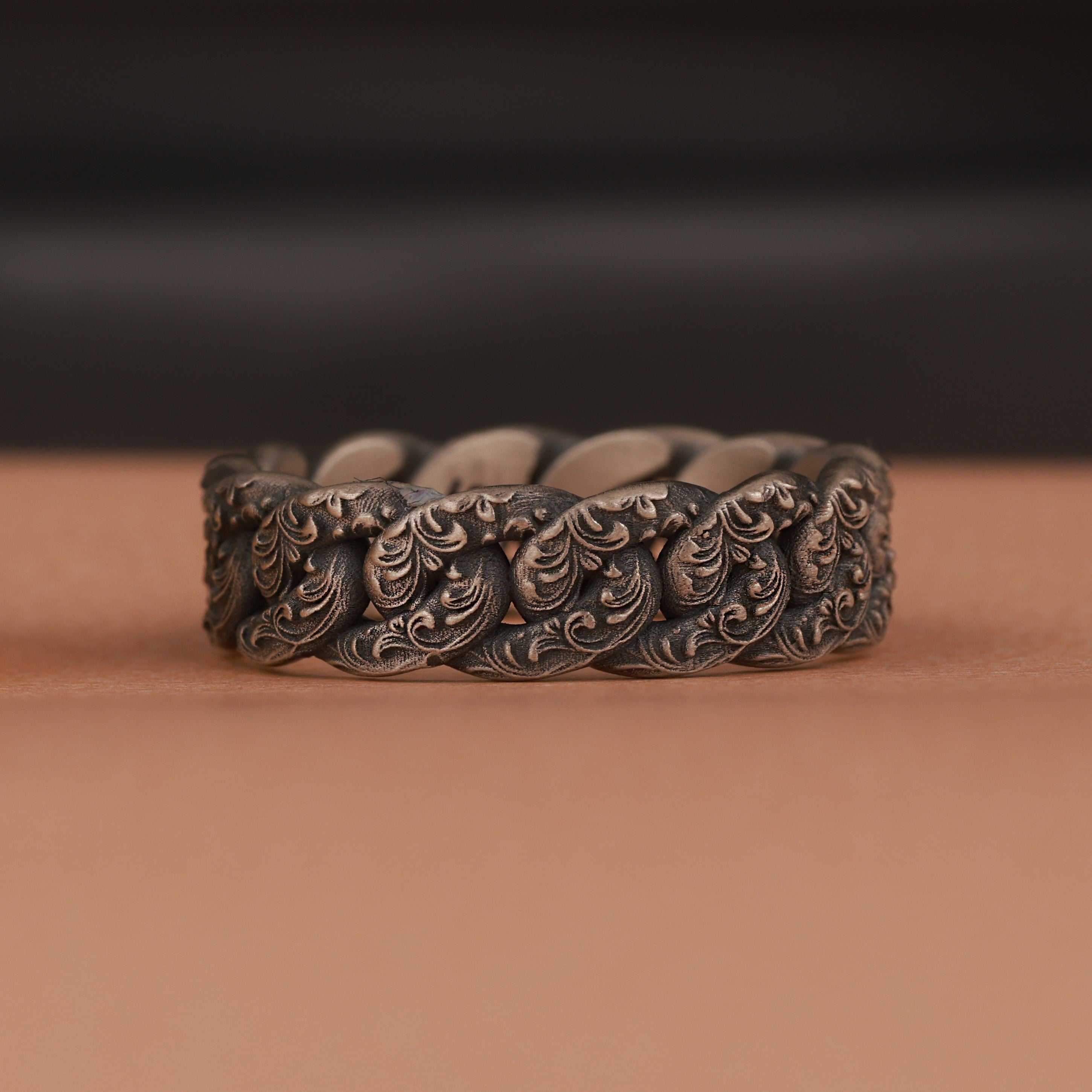 Floral silver chain ring on a brown surface with a blurred black background