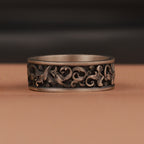 Decorative silver ring with intricate designs on a brown surface