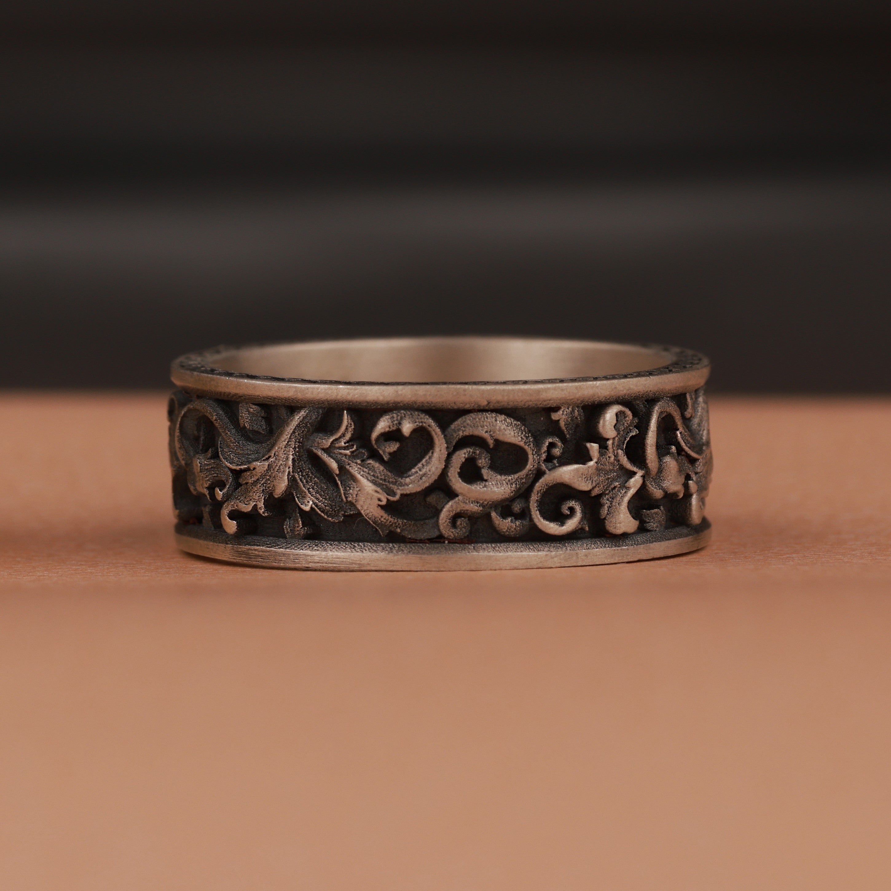 Decorative silver ring with intricate designs on a brown surface