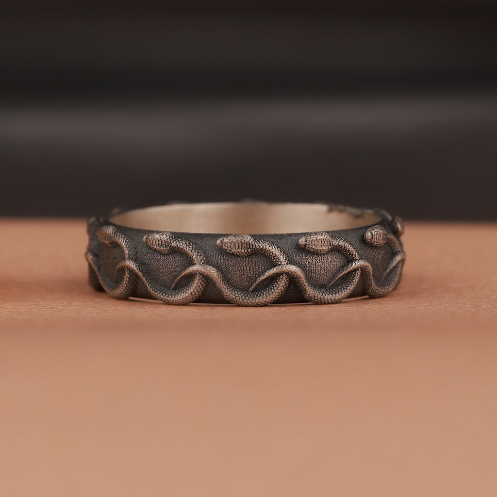 Decorative silver ring with engraved snake patterns on a brown surface