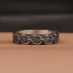 Decorative silver ring with engraved snake patterns on a brown surface