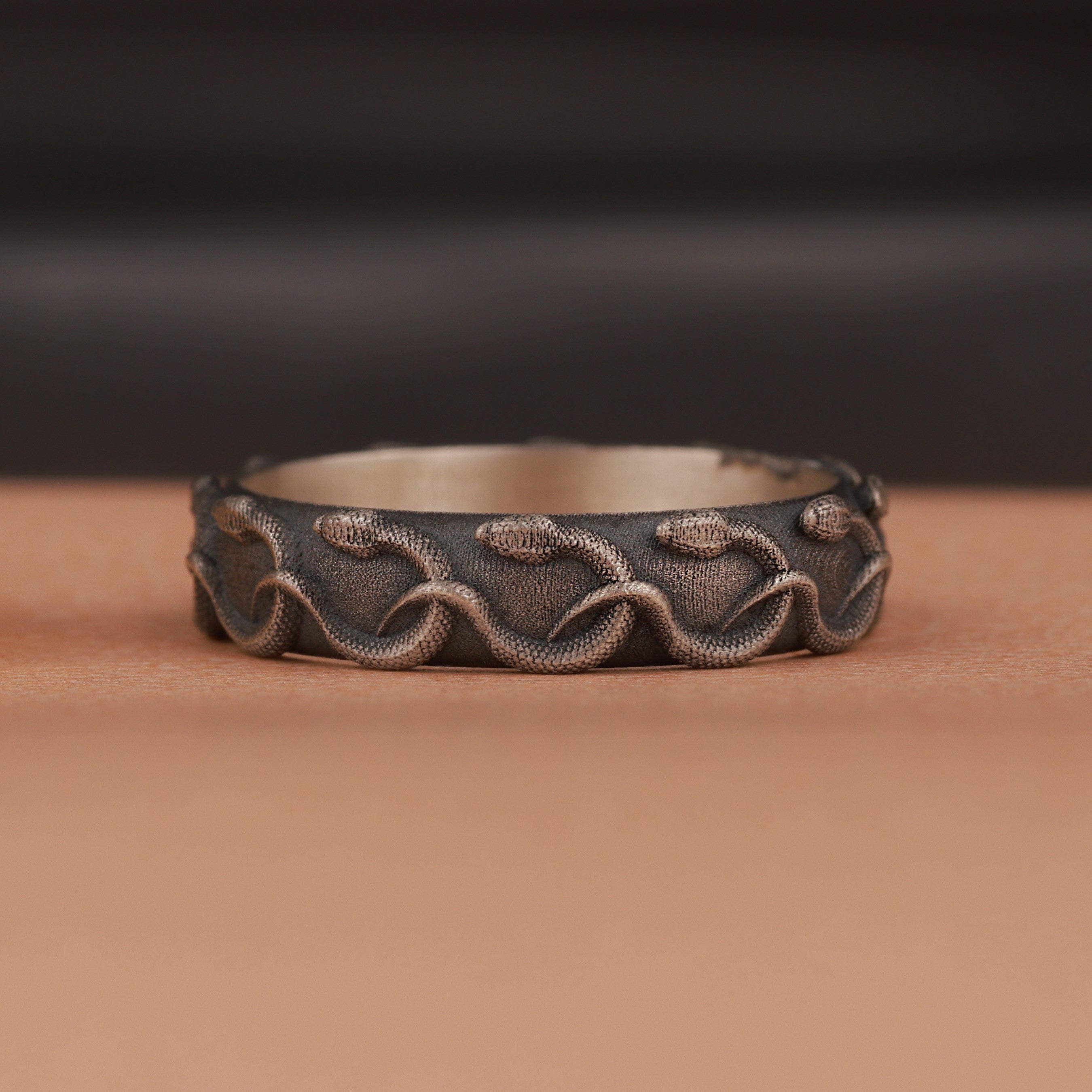 Decorative silver ring with engraved snake patterns on a brown surface