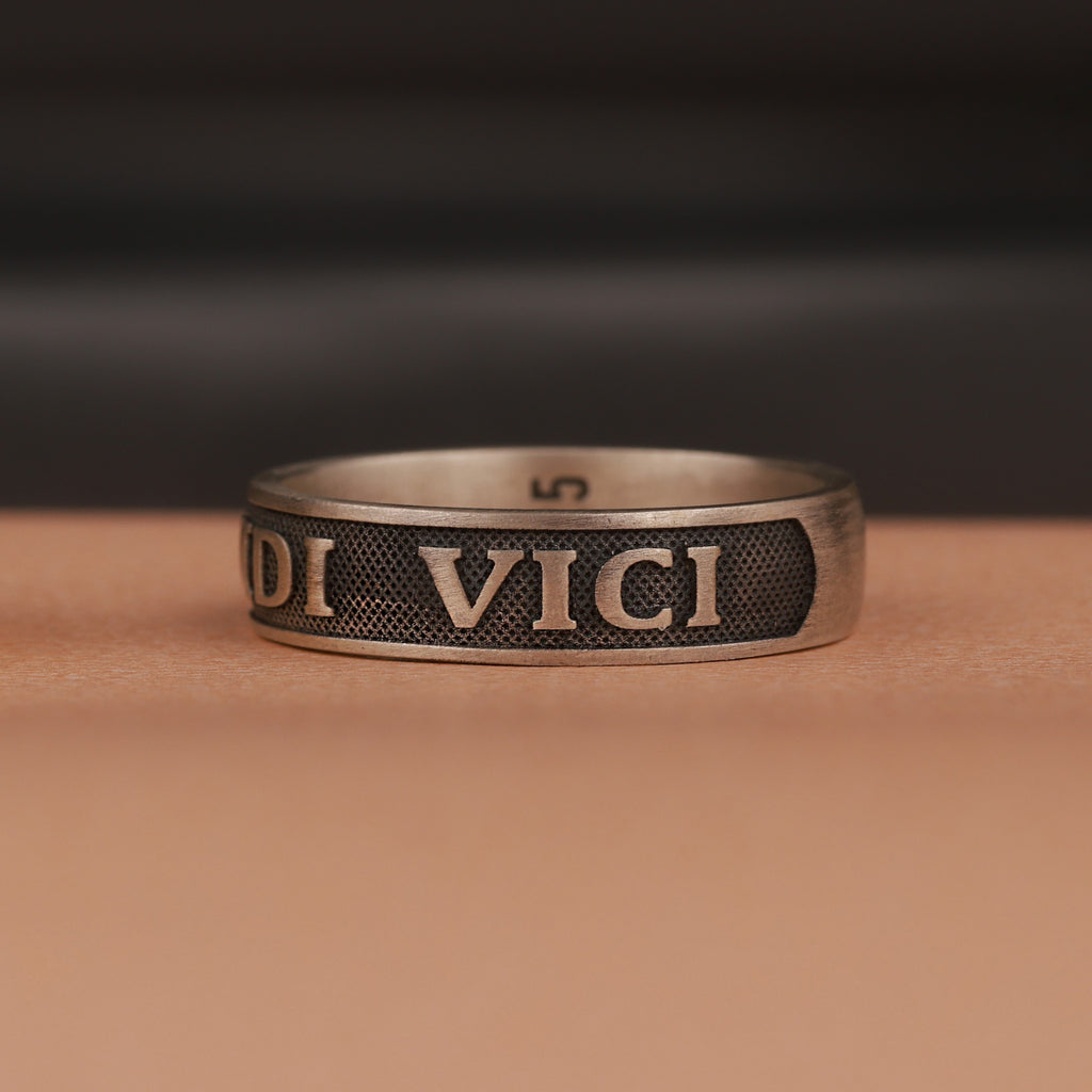 Bronze ring with 'veni vidi vici' engraving on a brown surface