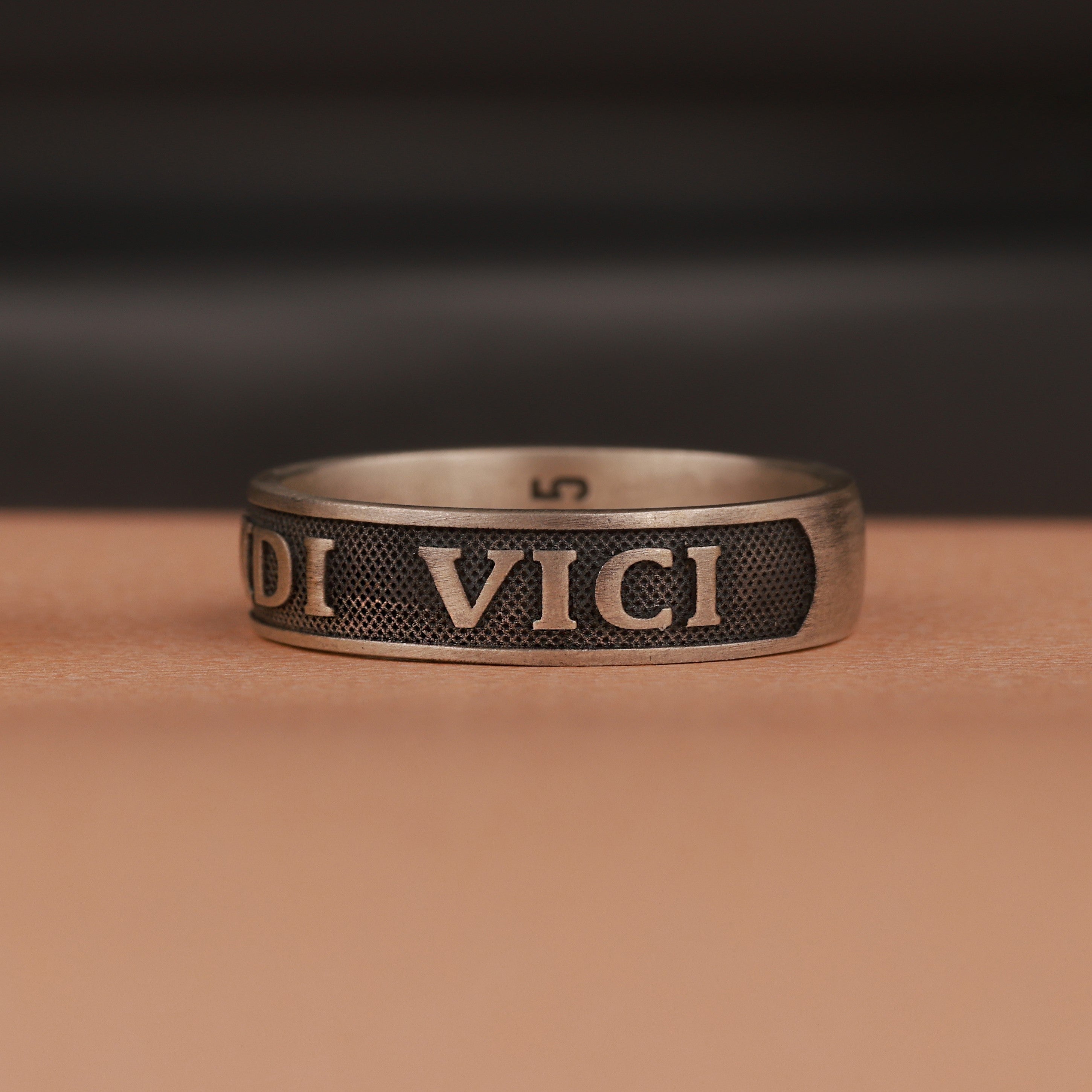 Bronze ring with 'veni vidi vici' engraving on a brown surface