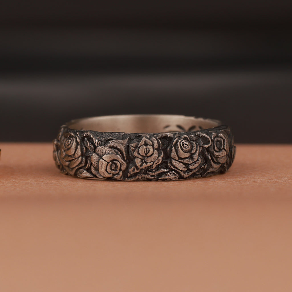 An oxidized silver ring with engraved rose flower motifs on brown surface