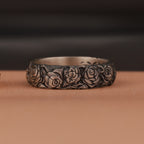 An oxidized silver ring with engraved rose flower motifs on brown surface