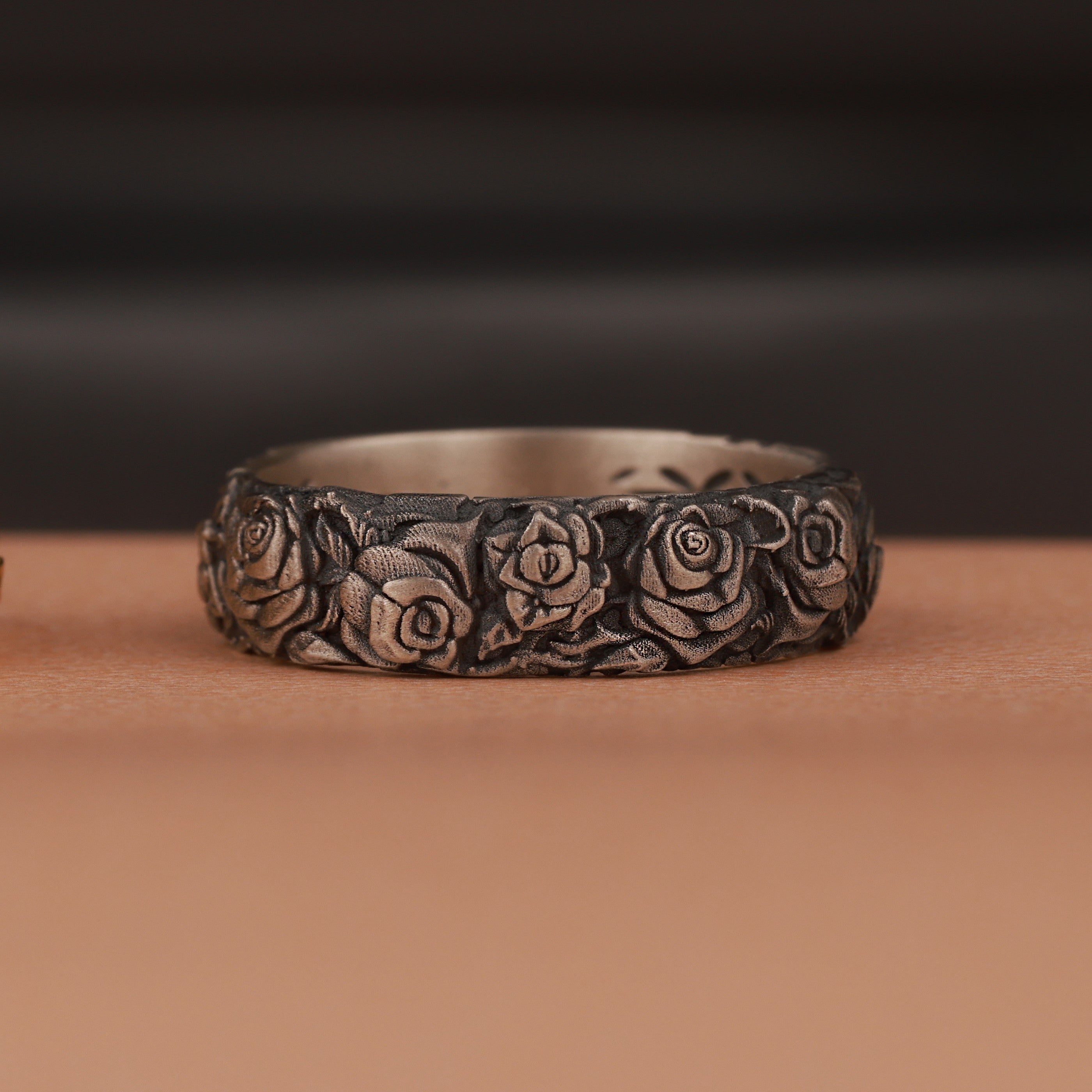An oxidized silver ring with engraved rose flower motifs on brown surface