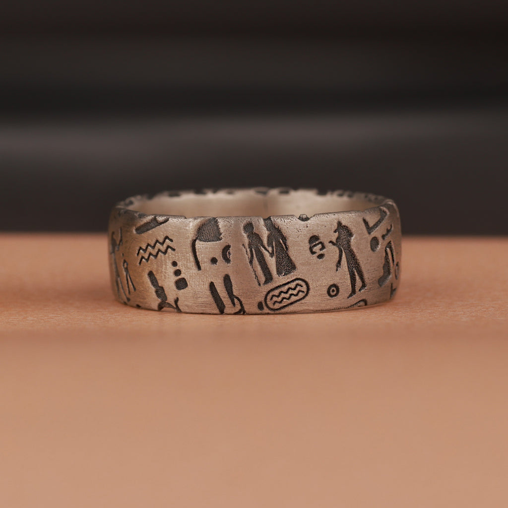 Silver ring with engraved Egyptian symbols on a brown surface