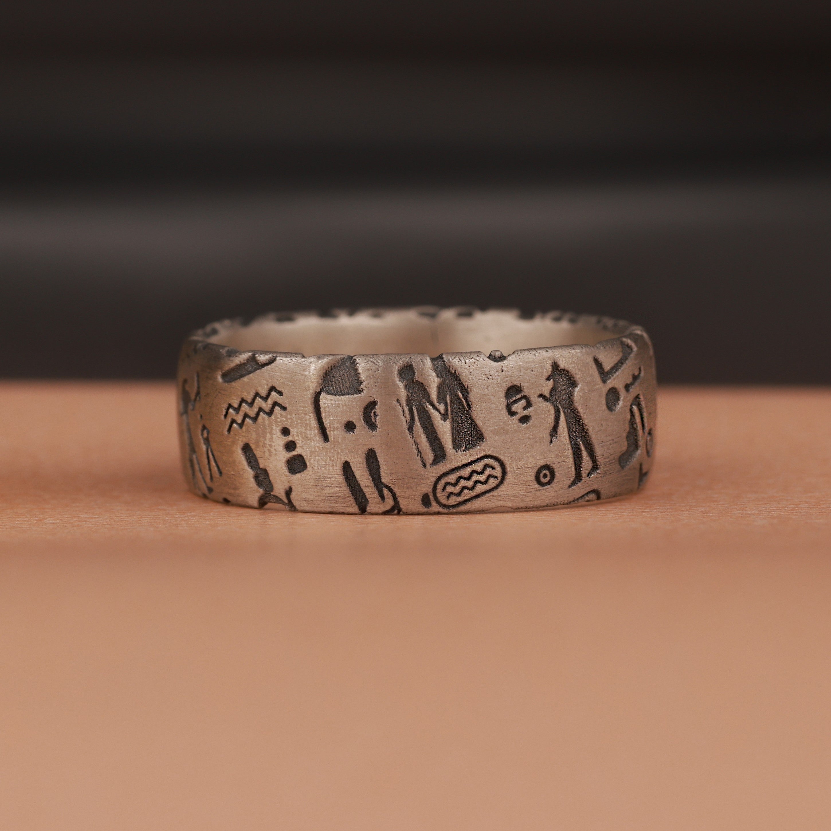 Silver ring with engraved Egyptian symbols on a brown surface