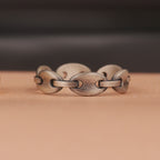 Oxidized silver chain-link ring on a wooden surface with a dark background