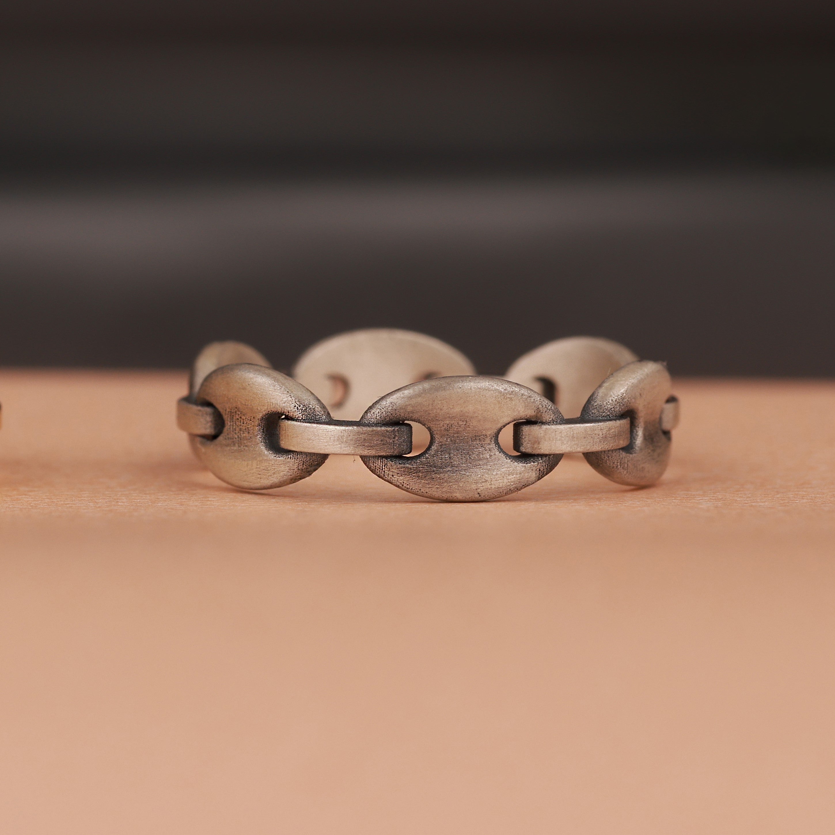 Oxidized silver chain-link ring on a wooden surface with a dark background