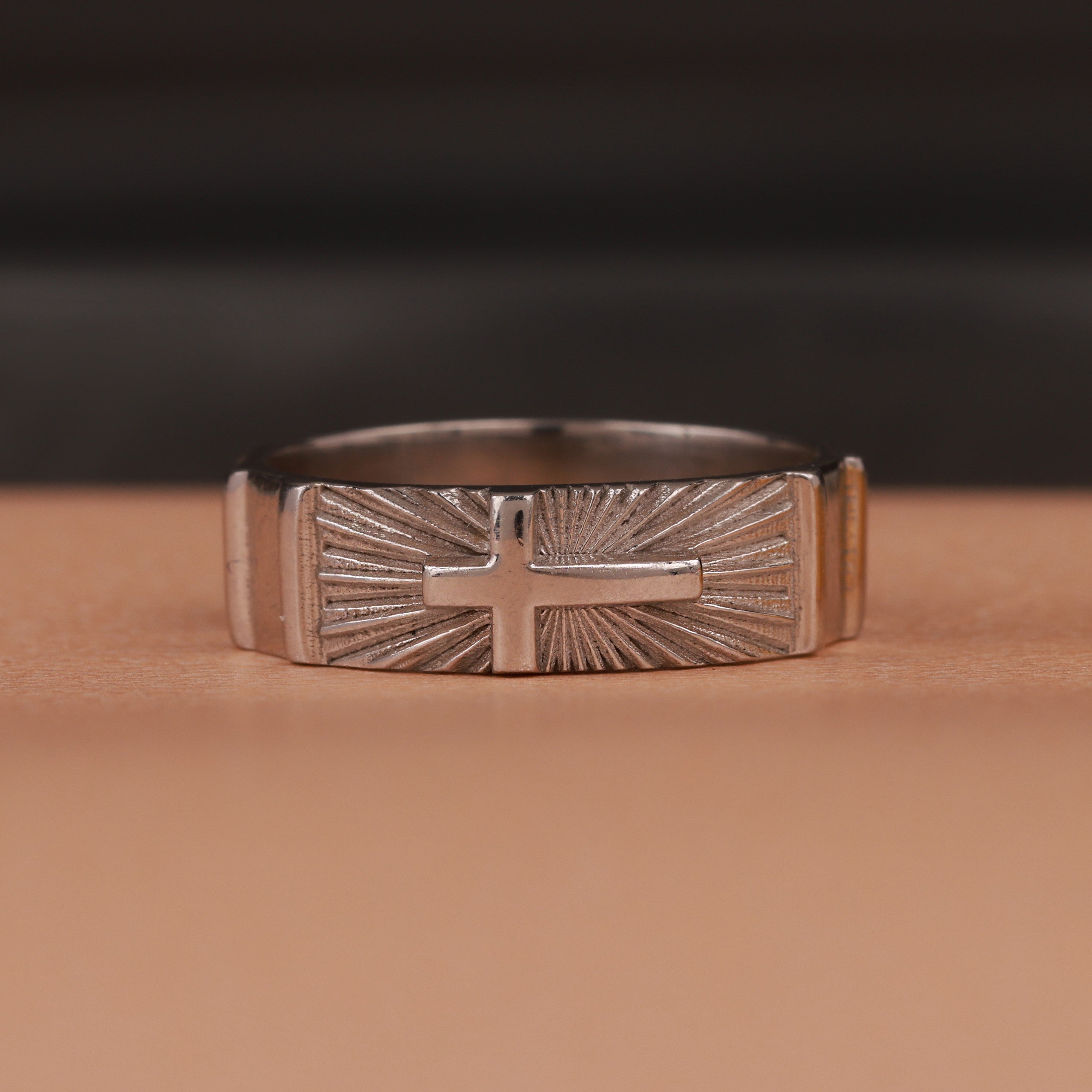 Polished silver ring with cross design on a brown background
