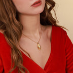 A close-up of a woman wearing a delicate gold chain necklace with a buddha pendant, styled with a vibrant red velvet top against a warm beige background.